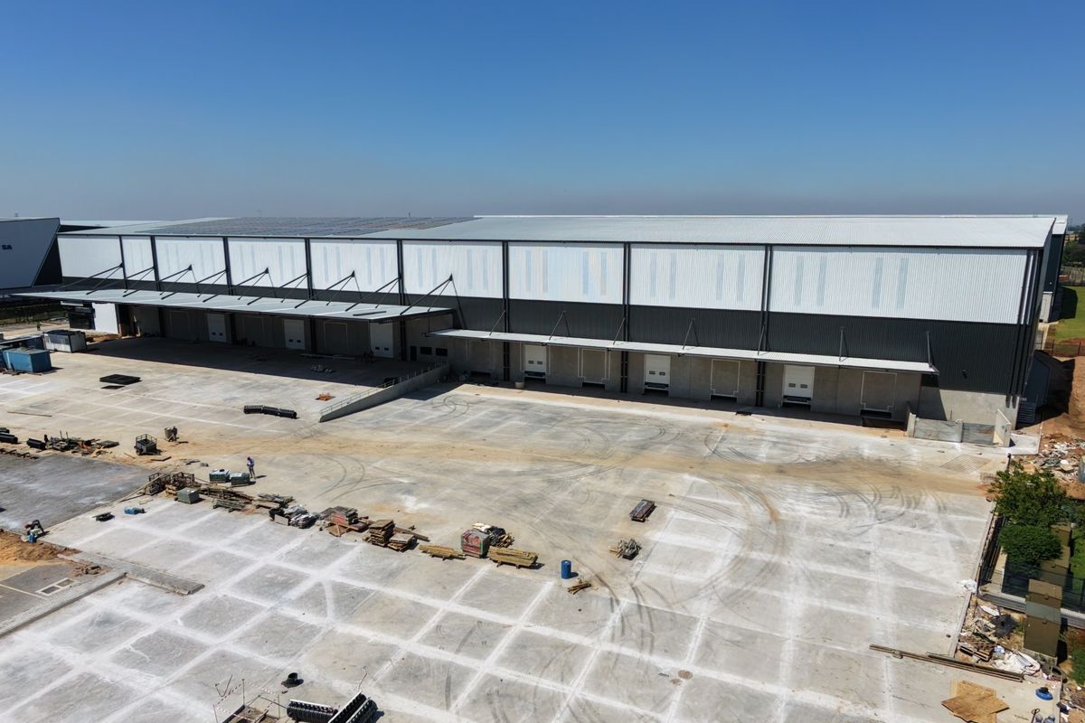 Aerial view of a large industrial warehouse facility featuring multiple loading docks, extensive concrete hardstand area, and roof-mounted solar panels.