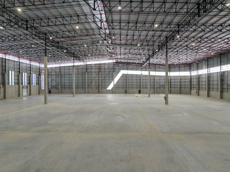 A spacious, modern industrial warehouse featuring high ceilings with exposed steel trusses, polished concrete flooring, and ample natural light through high-level windows.