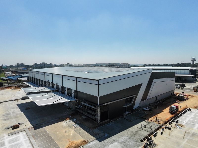 Aerial view of a modern industrial warehouse facility featuring a large metal roof with solar panels, loading bay canopies, and extensive concrete hardstand areas.