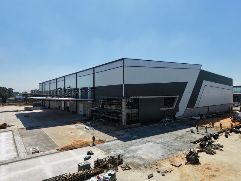 Aerial view of a large industrial warehouse facility under construction, featuring modern metal cladding, loading bays, and extensive concrete hardstand areas.