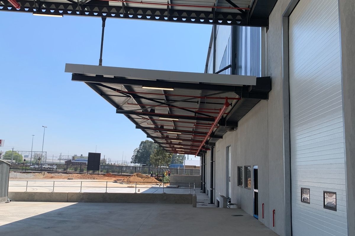Industrial loading bay area featuring a large roller shutter door, expansive concrete apron, and a covered steel canopy with integrated fire sprinkler systems.