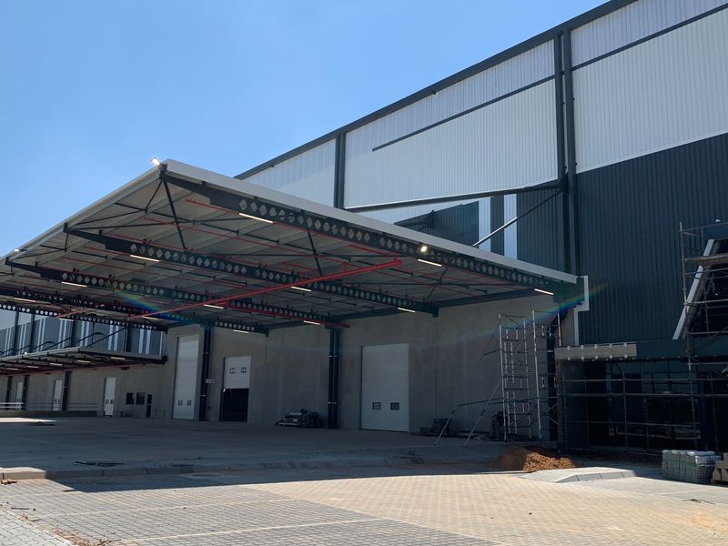 Modern industrial warehouse facility featuring a large concrete loading apron, multiple roller shutter doors, and an extensive overhead canopy structure.