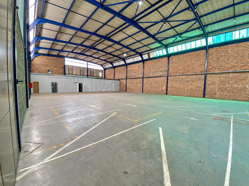 Spacious industrial warehouse featuring high-clearance steel truss roofing, exposed brick walls, and durable concrete flooring with marked utility zones.