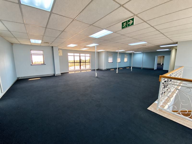 Spacious open-plan industrial office area featuring a suspended ceiling, recessed lighting, carpeted flooring, and a decorative wrought iron balustrade overlooking the lower level.