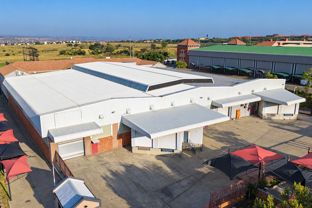 Aerial view of an industrial warehouse facility featuring a large corrugated metal roof, multiple loading bays with roller shutter doors, and a paved yard.