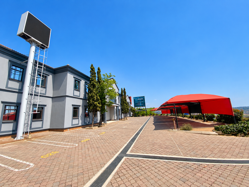 A well-maintained industrial property exterior featuring a paved parking area, covered parking bays, and a prominent digital billboard under a clear blue sky.