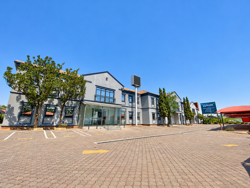 A well-maintained industrial office building featuring a paved parking lot, glass entrance, and prominent signage under a clear blue sky.
