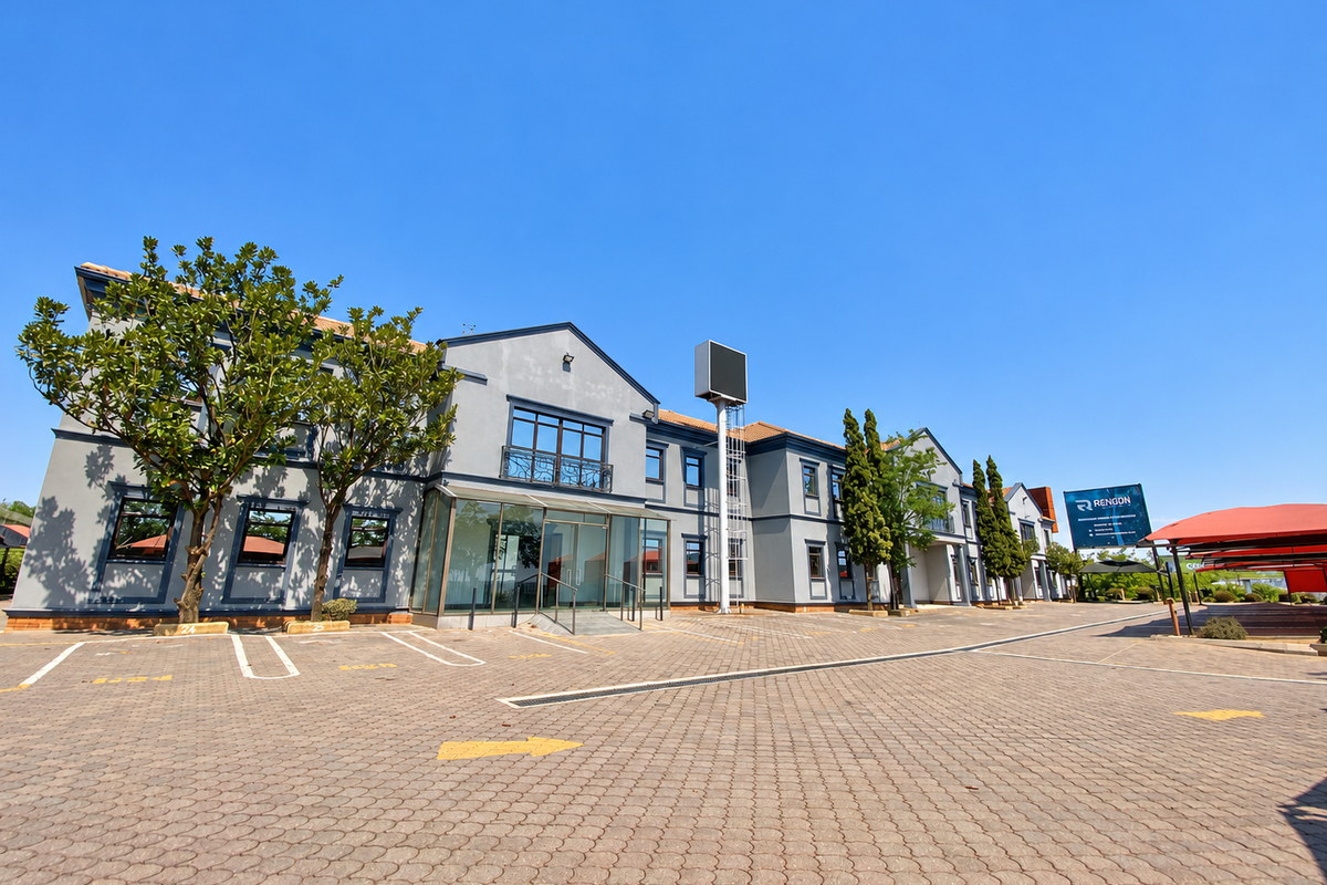 A well-maintained industrial office building featuring a paved parking lot, glass entrance, and prominent signage under a clear blue sky.