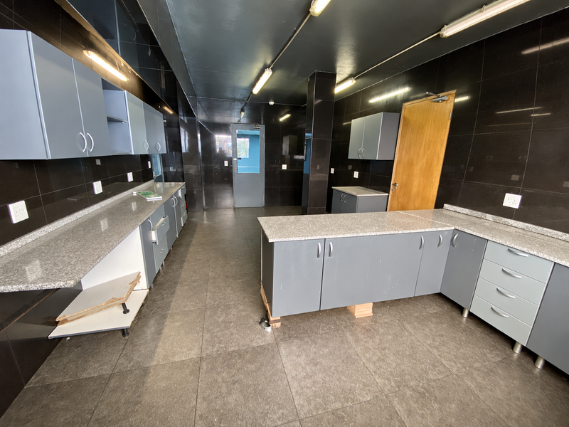 Industrial kitchen space featuring extensive grey cabinetry, granite countertops, dark tiled walls, and durable floor tiling, suitable for a functional workspace or staff area.