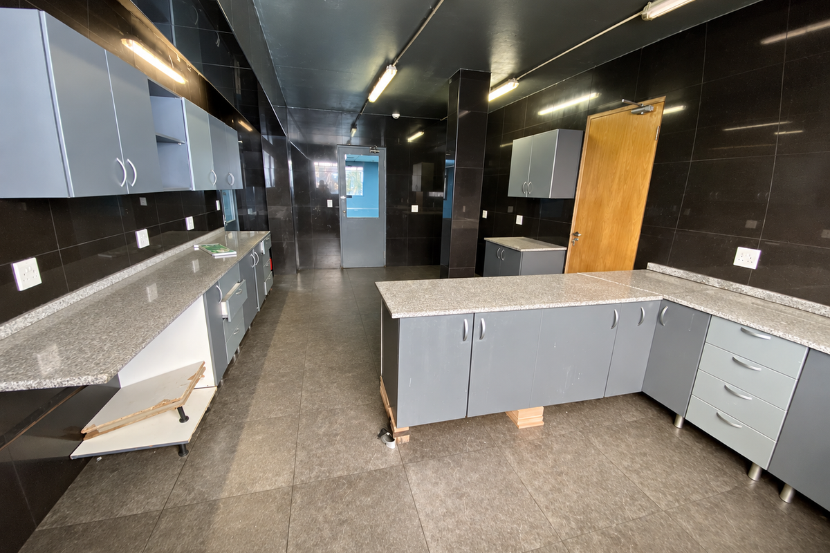 Industrial kitchen space featuring extensive grey cabinetry, granite countertops, dark tiled walls, and durable floor tiling, suitable for a functional workspace or staff area.