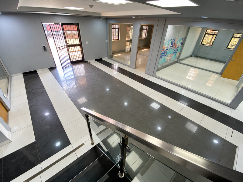 Spacious industrial hallway featuring modern tiled flooring, glass partitions, and a stainless steel balustrade, providing a clean and professional office environment.