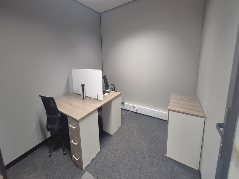 A compact, well-maintained office space featuring neutral grey walls, carpeted flooring, and integrated electrical trunking for connectivity.