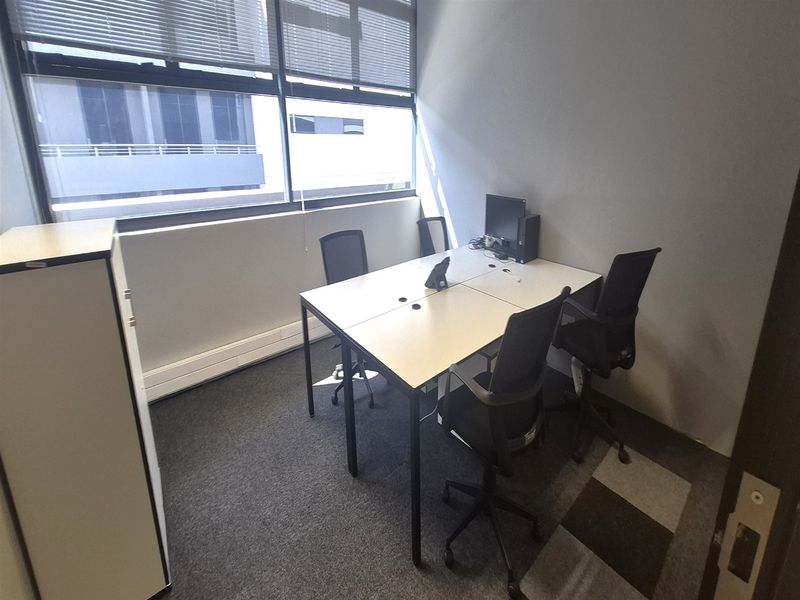 A functional office space featuring carpeted flooring, a large window with venetian blinds, and built-in storage cabinetry.