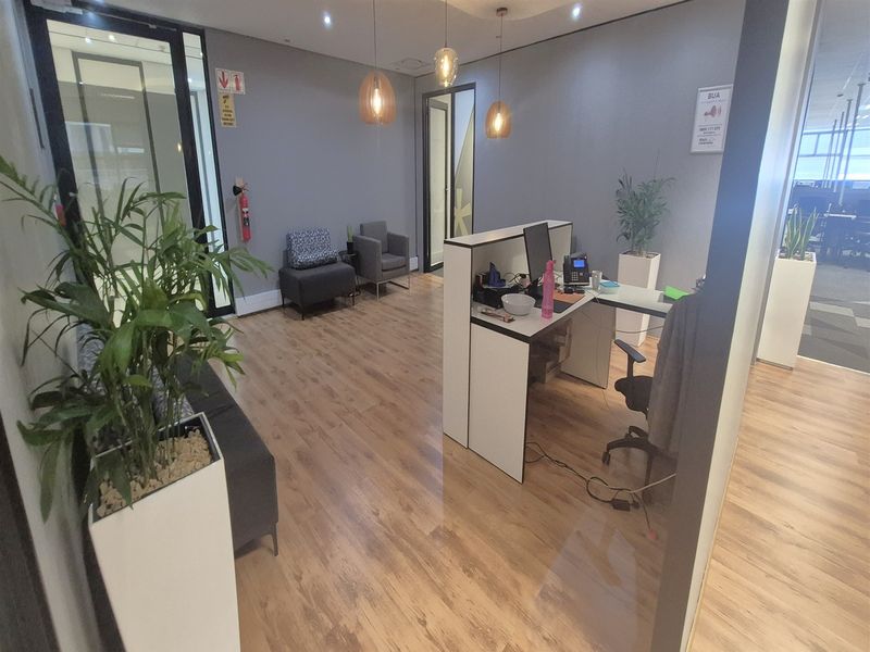 A modern office reception area featuring laminate wood flooring, recessed ceiling lighting, and a functional built-in reception desk with glass partition walls.
