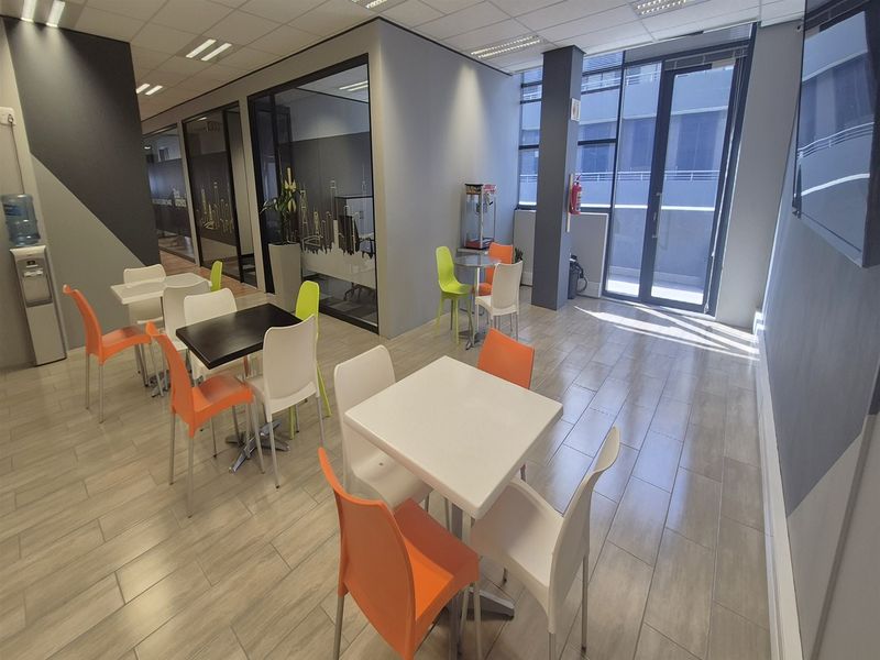 Modern office break-out area featuring tiled flooring, suspended ceilings, and glass partition walls, providing a bright and professional workspace environment.