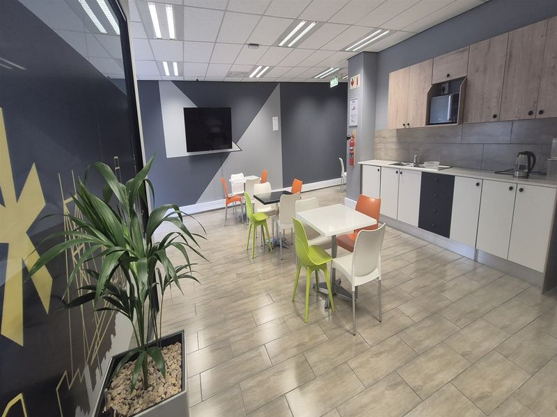 A modern office kitchenette featuring built-in cabinetry, laminate countertops, a stainless steel sink, and tiled flooring, suitable for staff breakroom use.