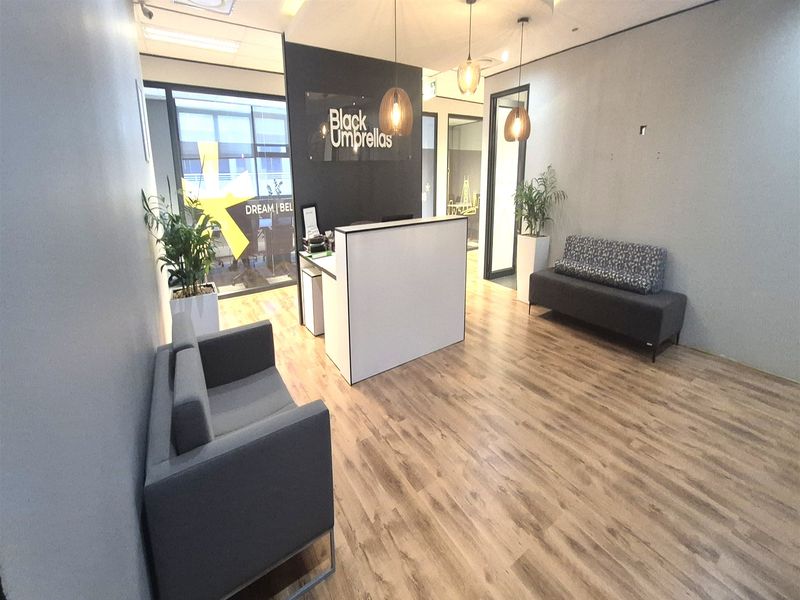 Modern office reception area featuring laminate flooring, glass partitions, and contemporary pendant lighting, creating a professional and welcoming entrance for clients.