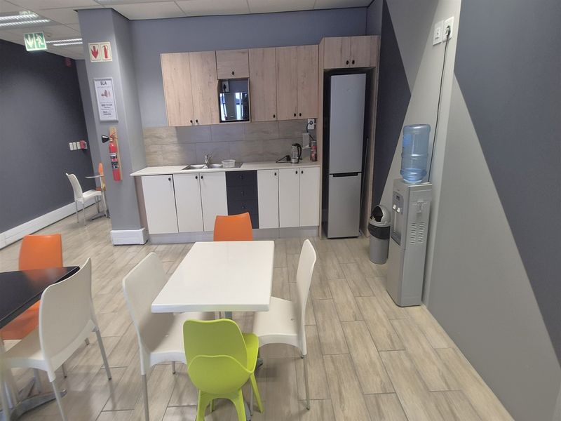 A functional office kitchenette featuring built-in cabinetry, a stainless steel sink, tiled backsplash, and durable wood-look floor tiles.