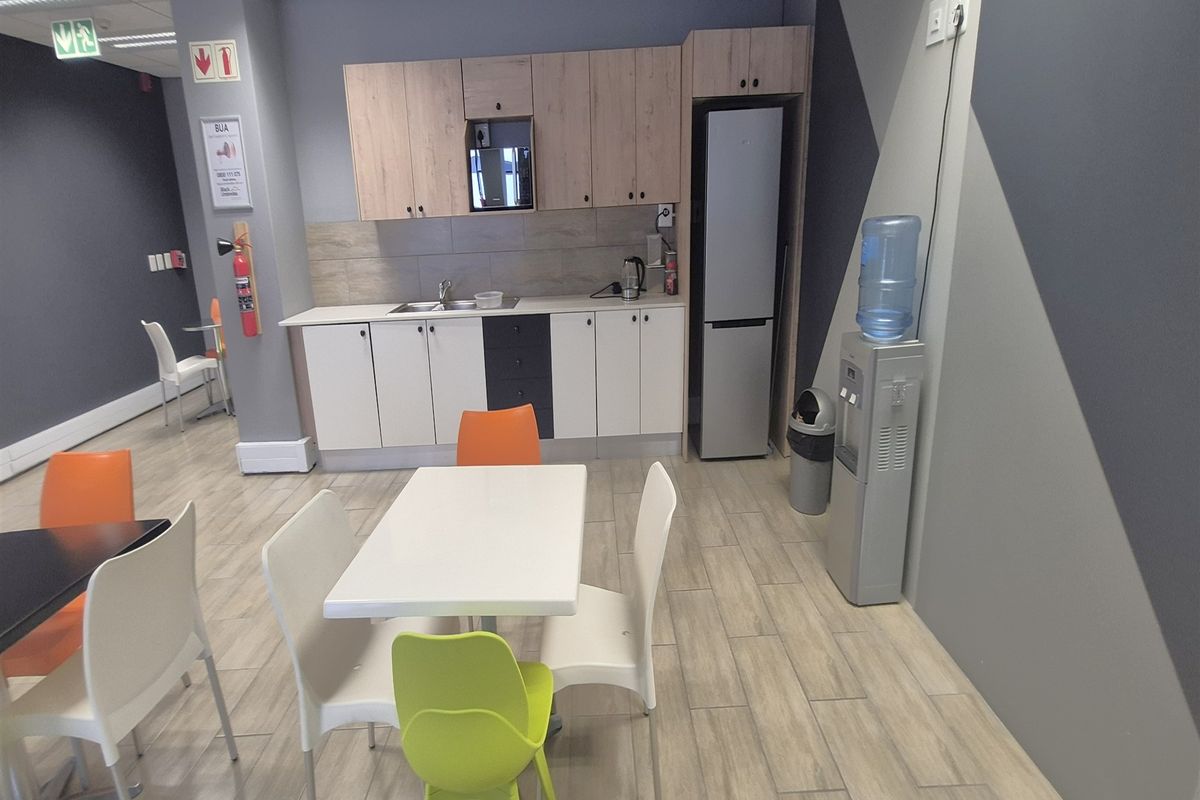 A functional office kitchenette featuring built-in cabinetry, a stainless steel sink, tiled backsplash, and durable wood-look floor tiles.