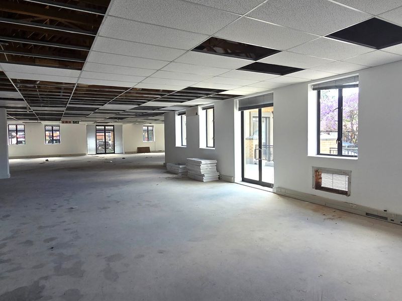 Spacious open-plan office area currently undergoing renovation, featuring exposed ceiling grid, concrete floors, and large windows providing ample natural light.