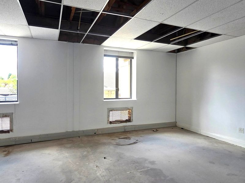 An empty office space requiring renovation, featuring exposed ceiling grid, unfinished concrete floors, and wall-mounted ventilation openings.