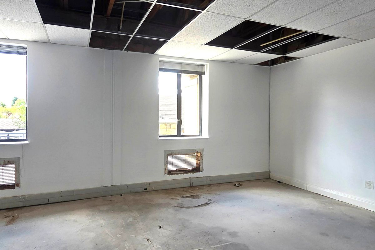 An empty office space requiring renovation, featuring exposed ceiling grid, unfinished concrete floors, and wall-mounted ventilation openings.