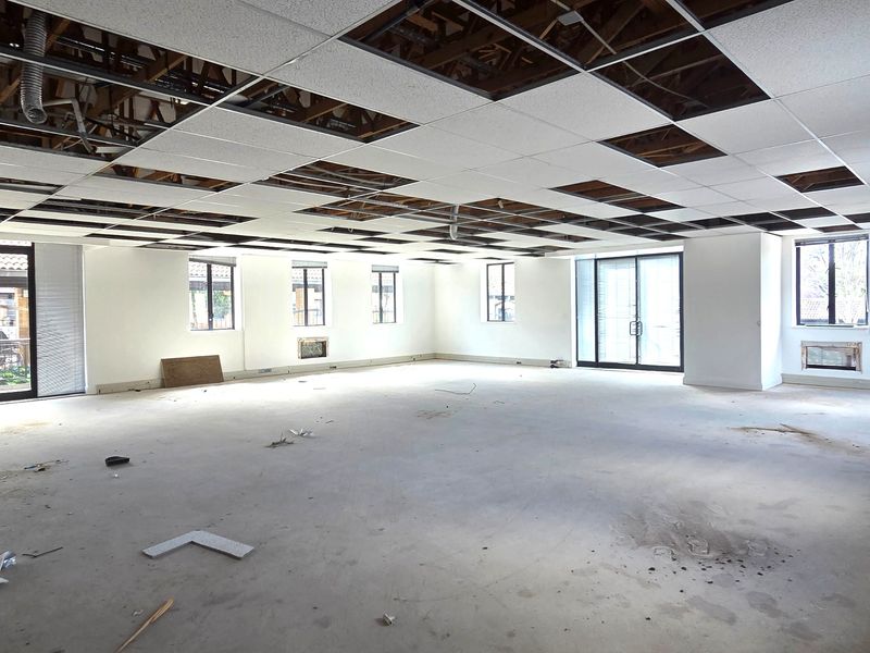 Spacious open-plan office area featuring large windows, sliding glass doors, and a suspended ceiling grid requiring completion.