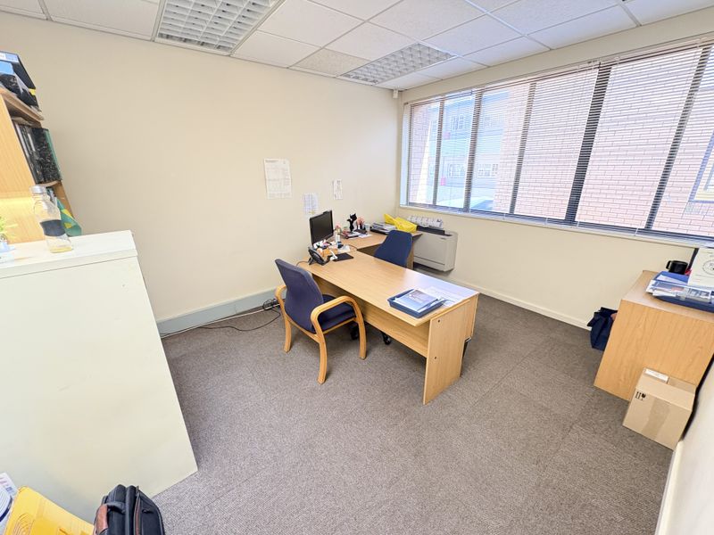 A functional office space featuring a suspended ceiling, carpeted flooring, and large windows with venetian blinds, providing ample natural light.