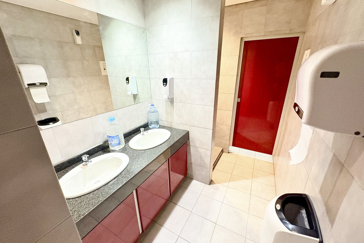 A functional office bathroom featuring a double vanity with integrated sinks, large wall-mounted mirror, and neutral tiled finishes throughout.