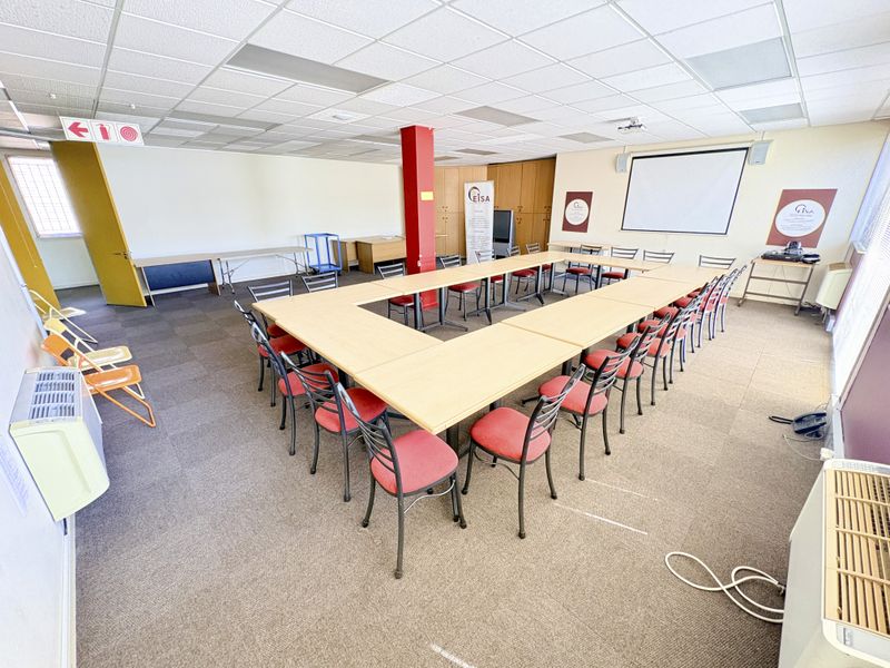 Spacious office meeting room featuring a suspended ceiling, built-in storage cabinetry, a projector screen, and wall-mounted air conditioning units.