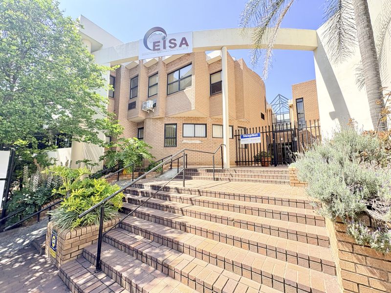 Front entrance of the office building featuring a brick facade, paved staircase with metal handrails, and secure gated access.