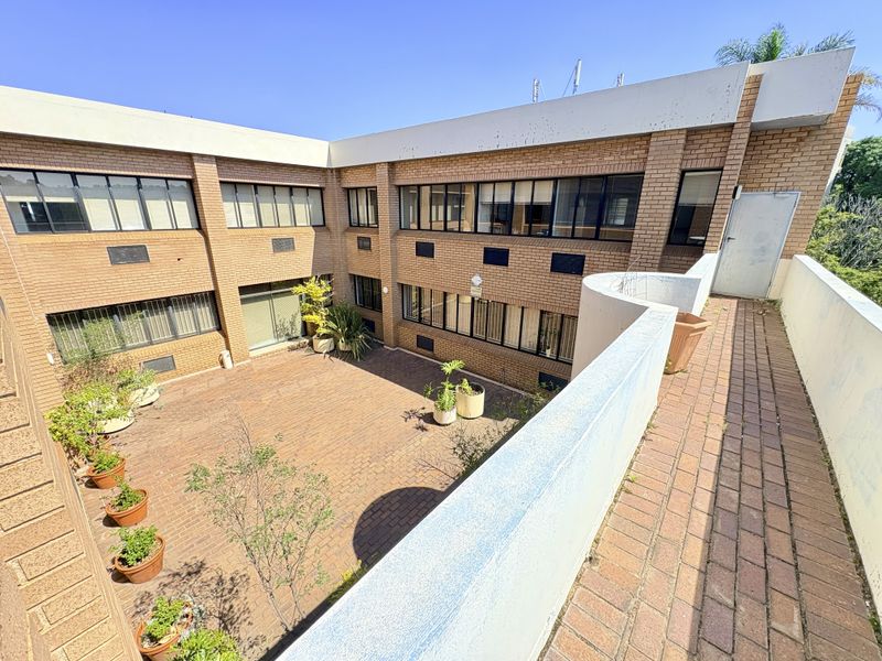 An exterior view of a brick office building featuring a paved central courtyard and an elevated balcony area.