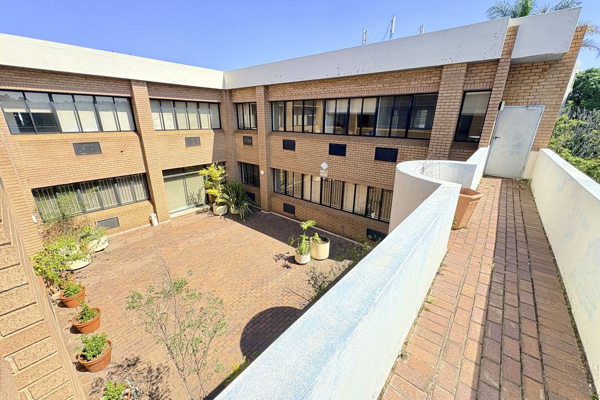 An exterior view of a brick office building featuring a paved central courtyard and an elevated balcony area.