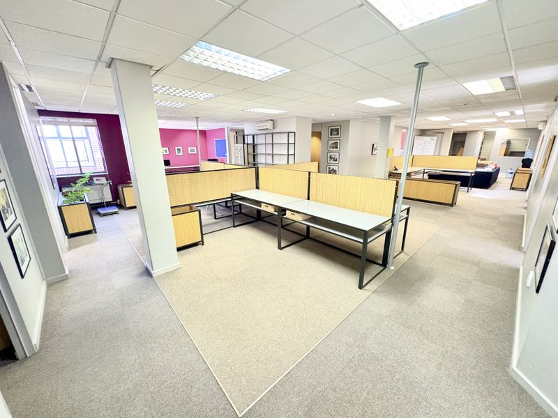 Open-plan office space featuring carpeted flooring, suspended ceilings with recessed lighting, and built-in workstation partitions for a functional professional environment.