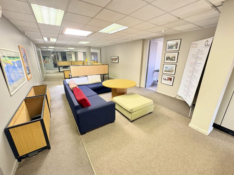 A spacious open-plan office area featuring suspended ceilings, recessed lighting, and neutral carpeting, currently configured with a lounge seating area.