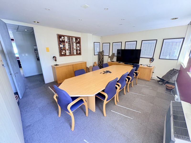 A functional office boardroom featuring recessed lighting, carpeted flooring, and a wall-mounted heater, providing a professional space for meetings and collaborative work.