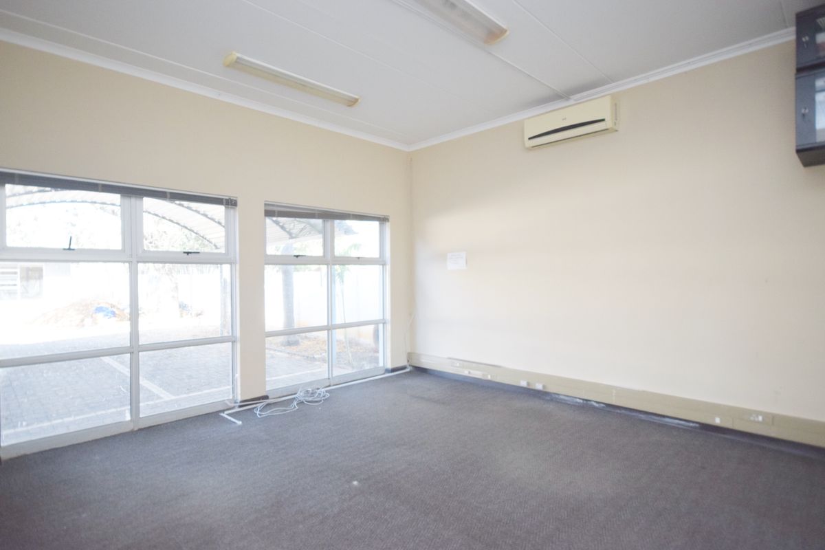 An empty office space featuring carpet flooring, large aluminium windows, and a wall-mounted split-system air conditioner.