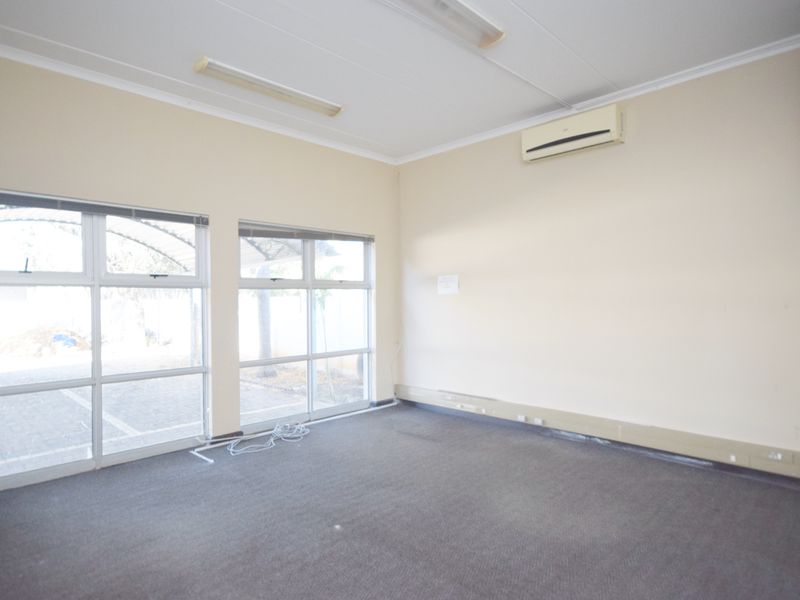 An empty office space featuring carpet flooring, large aluminium windows, and a wall-mounted split-system air conditioner.