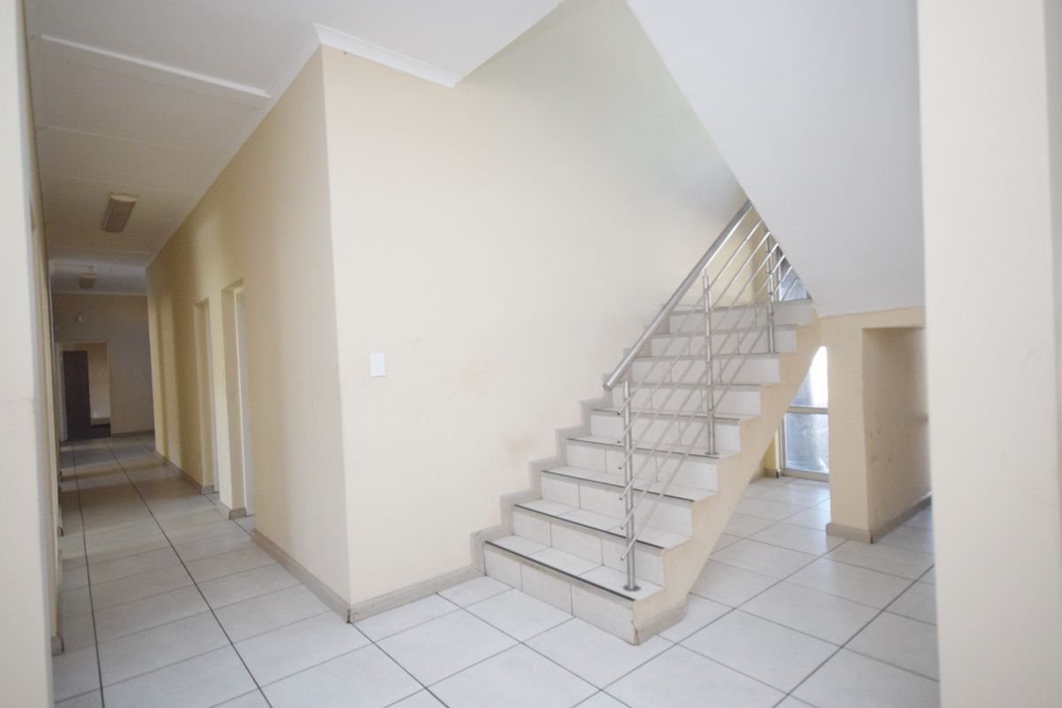 Spacious office hallway featuring tiled flooring and a staircase with a modern stainless steel railing, providing access to multiple office suites.