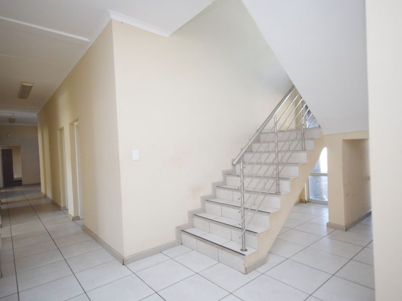 Spacious office hallway featuring tiled flooring and a staircase with a modern stainless steel railing, providing access to multiple office suites.