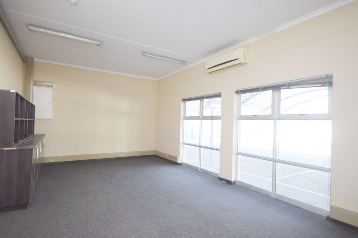 A bright, empty office space featuring carpet flooring, built-in cabinetry, large windows for natural light, and a wall-mounted air conditioning unit.
