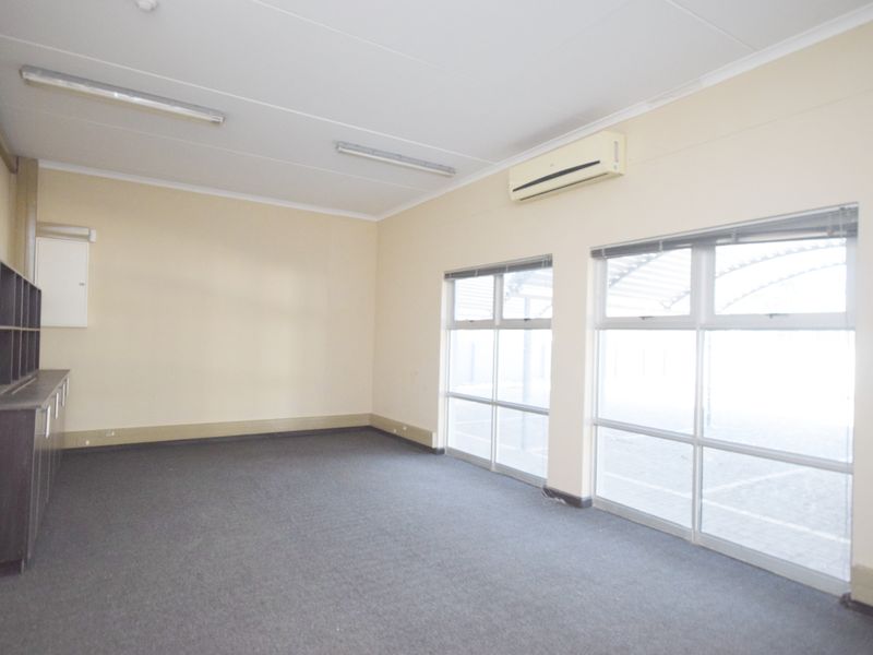 A bright, empty office space featuring carpet flooring, built-in cabinetry, large windows for natural light, and a wall-mounted air conditioning unit.