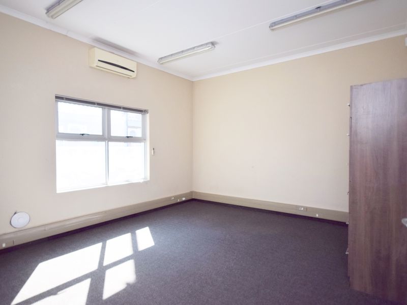 A clean, empty office space featuring carpeted flooring, split-system air conditioning, and functional fluorescent lighting, suitable for a professional workspace.