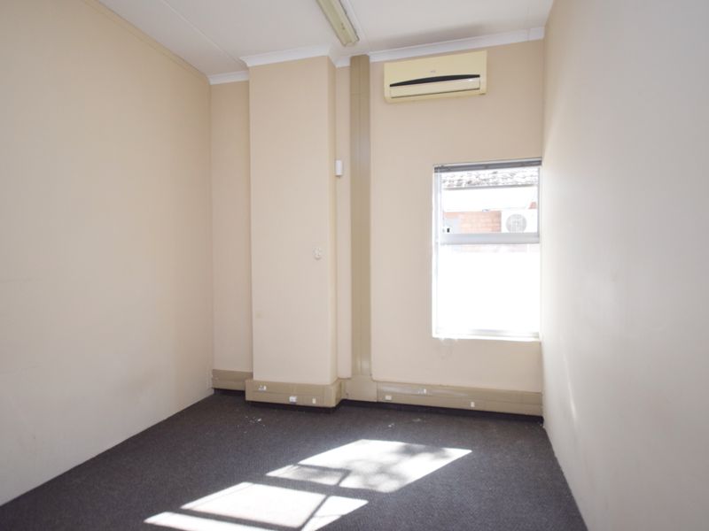 A clean, empty office space featuring neutral walls, carpet flooring, and a wall-mounted split-system air conditioning unit.