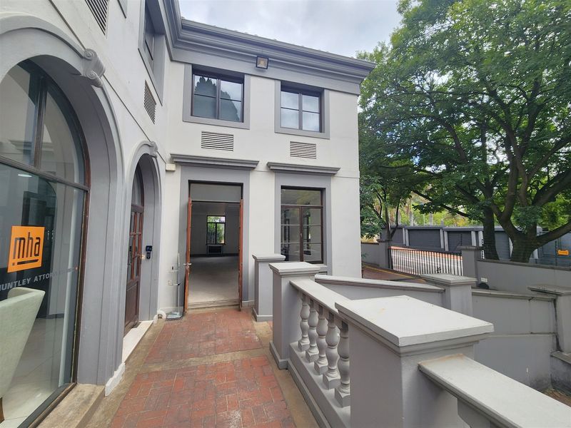 A well-maintained office building entrance featuring a brick-paved walkway, classic architectural archways, and a decorative balustrade.