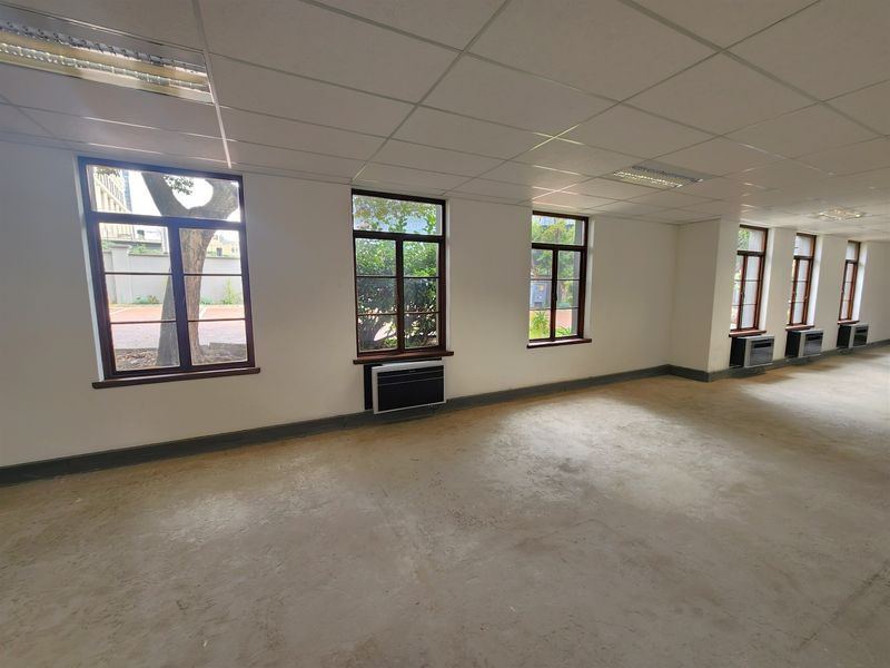 Spacious open-plan office area featuring a suspended ceiling, recessed lighting, multiple timber-framed windows, and integrated under-window air conditioning units.