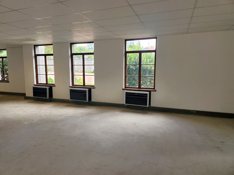 A spacious, empty office area featuring a suspended ceiling, timber-framed windows, and multiple wall-mounted air conditioning units, ready for custom fit-out.