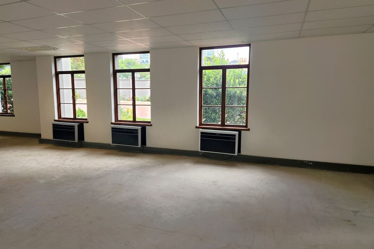 A spacious, empty office area featuring a suspended ceiling, timber-framed windows, and multiple wall-mounted air conditioning units, ready for custom fit-out.