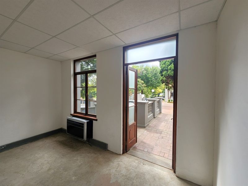 An empty office space featuring a suspended ceiling, concrete flooring, and direct access to an outdoor patio area through a timber frame door.