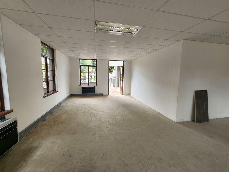 An empty, open-plan office space featuring a suspended ceiling, recessed lighting, and large windows, currently awaiting flooring installation and final finishes.
